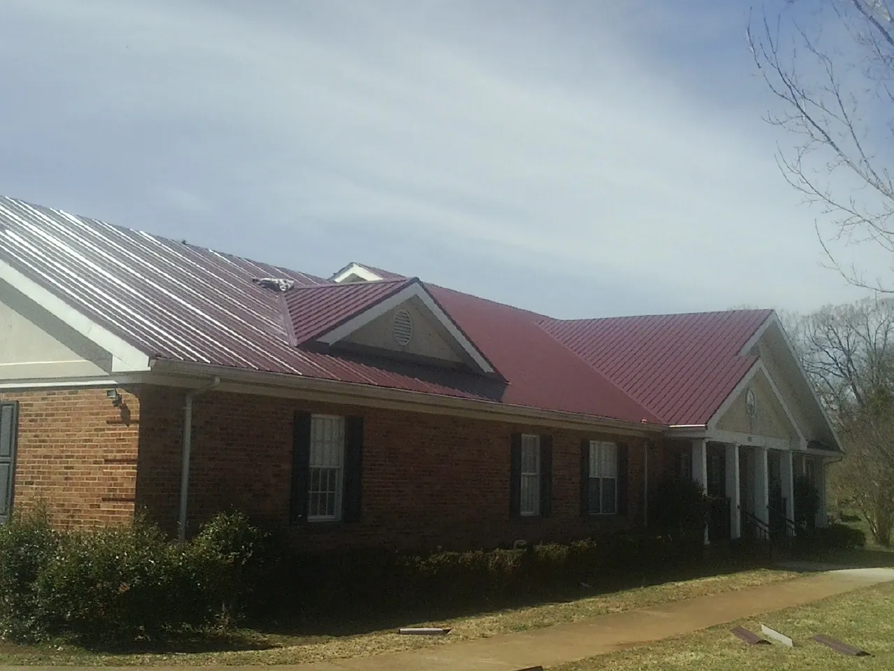 Red metal roof with gabled entries on a long brick building, from a Hail Damage Roof Repair job in Pocomoke City