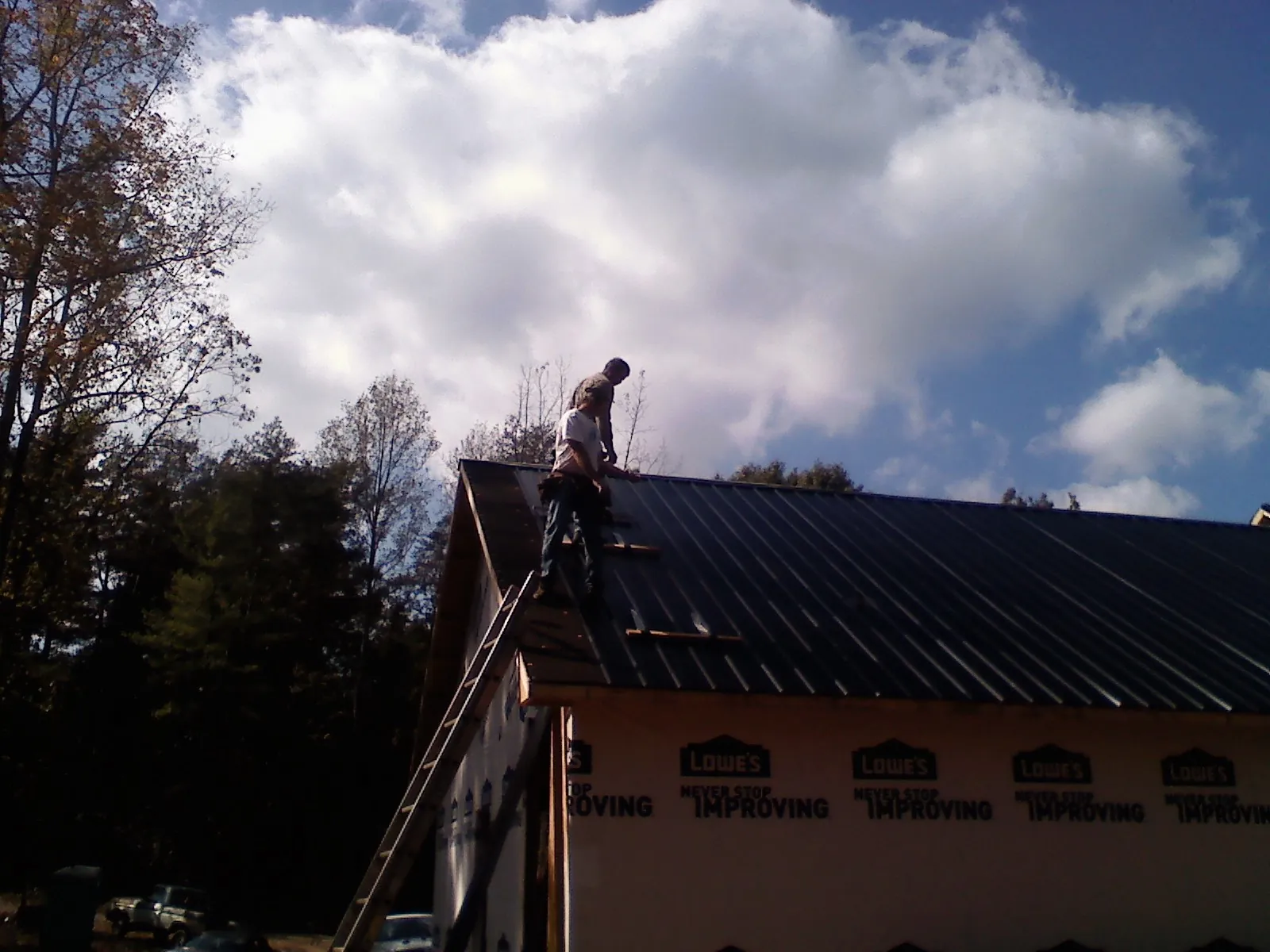 Roofer fastening dark metal panels high against a cloudy sky, from a Roof Inspection job in Pocomoke City