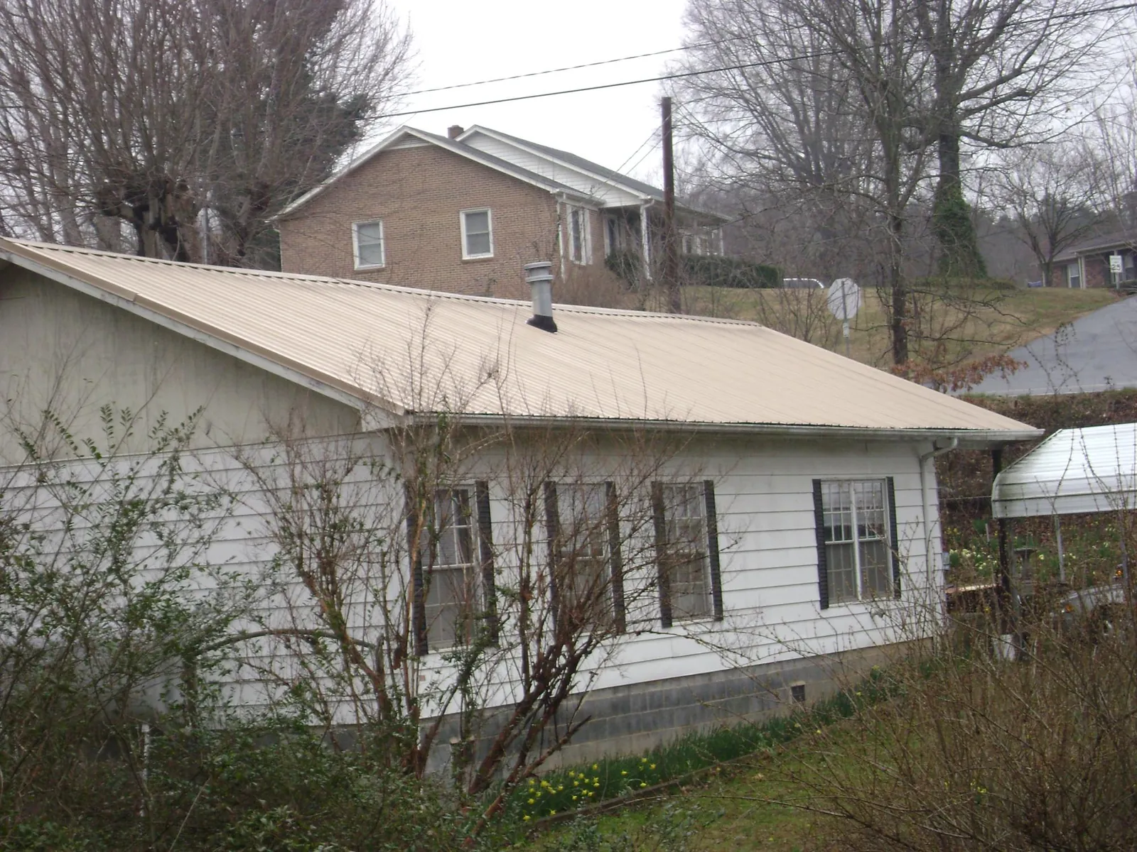 Tan metal roof on a white sided house set into a hillside — Commercial Roofing by Roofing Brothers in Pocomoke City